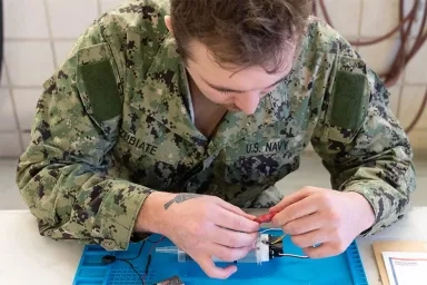 Naval sailor finessing wiring during advanced robotics training at Carnegie Mellon.